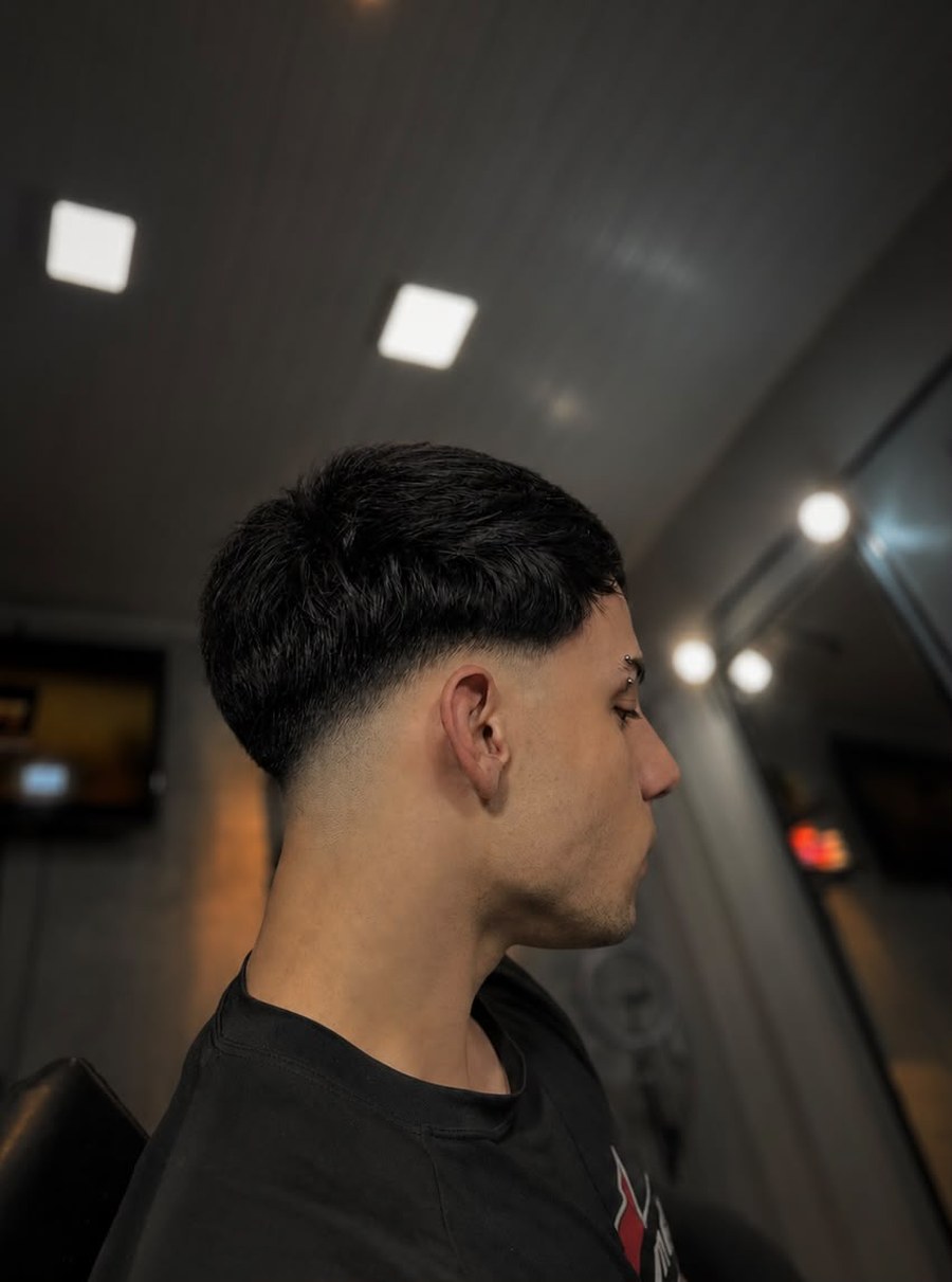 Cliente de perfil com corte de franja reta e degradê baixo nas laterais