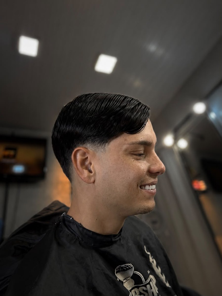 Cliente sorrindo com corte clássico penteado para o lado e acabamento alinhado